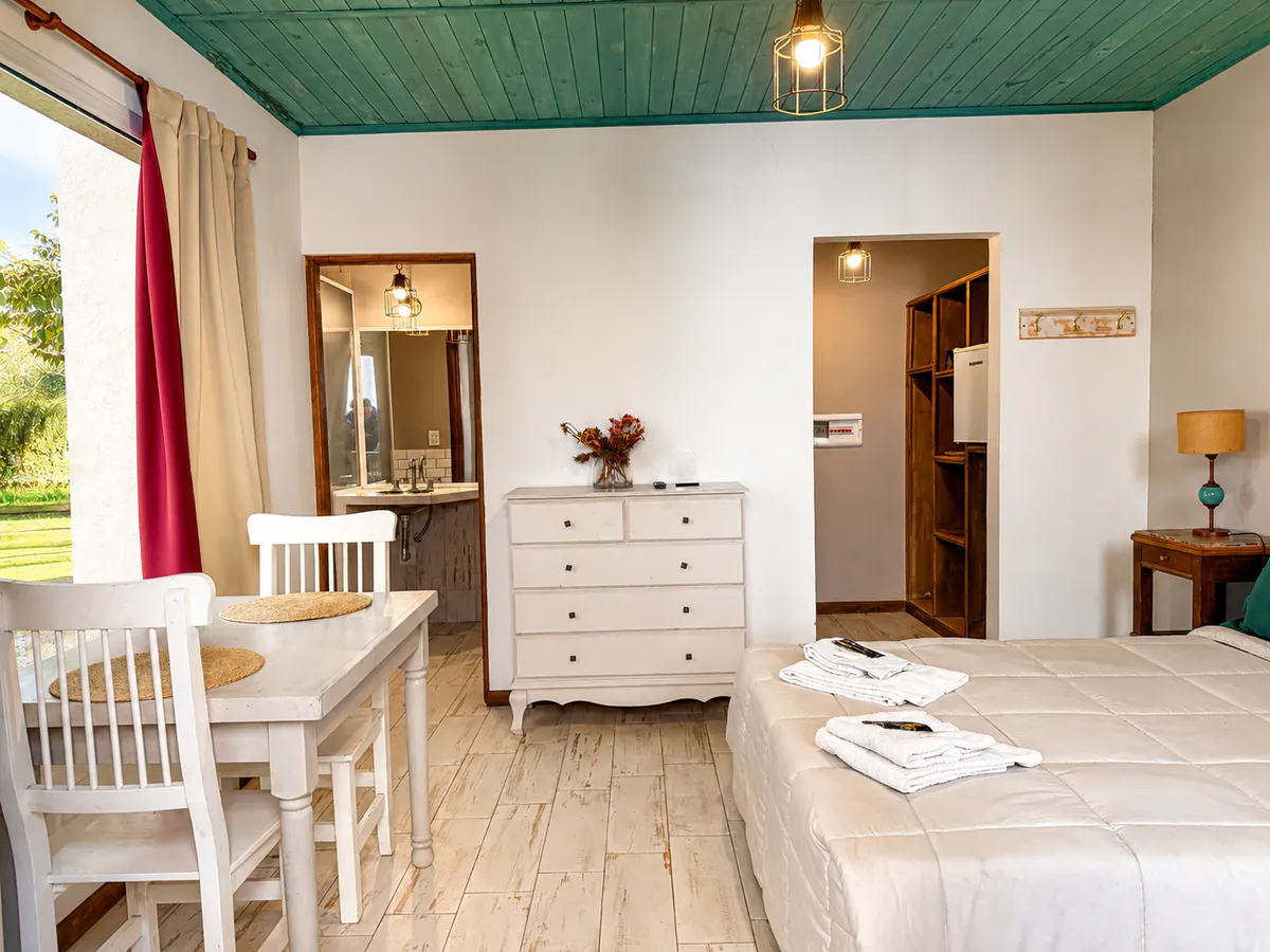 Ambiente de la Suite 12 con techo de madera verde, mesa para dos y cama matrimonial